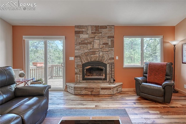 living room with healthy amount of natural light, wood finished floors, a stone fireplace, and baseboards