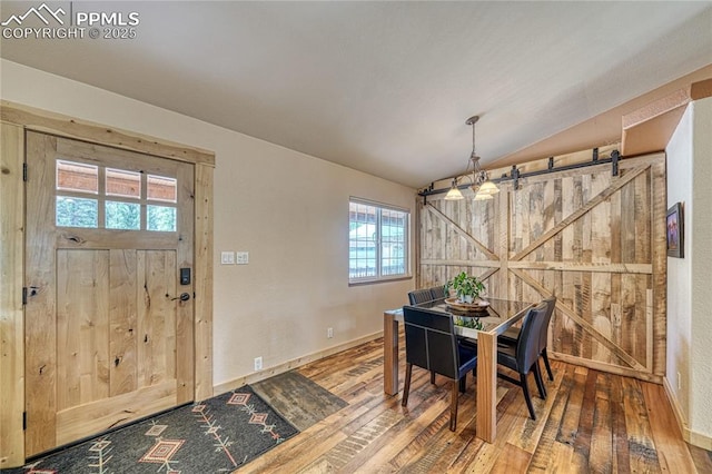 dining space featuring wood-type flooring, lofted ceiling, plenty of natural light, a barn door, and baseboards