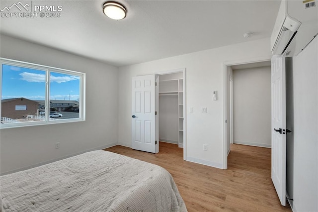 bedroom featuring a wall mounted air conditioner, light wood-style floors, baseboards, a walk in closet, and a closet
