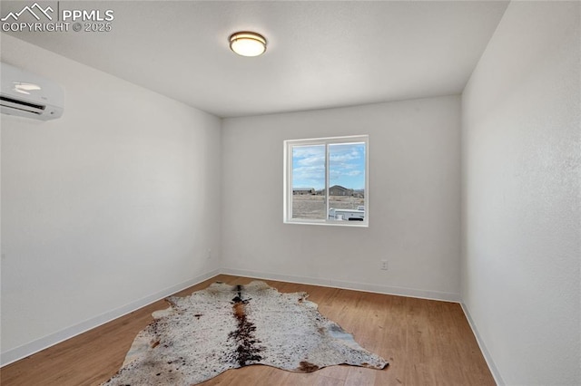 unfurnished room with a wall unit AC, wood finished floors, and baseboards