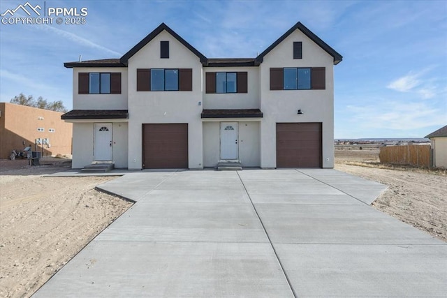 view of front of property with driveway, stucco siding, an attached garage, and fence