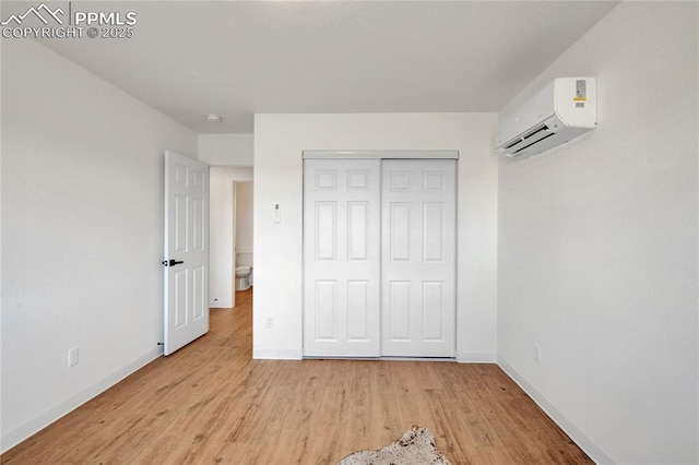 unfurnished bedroom with a wall mounted AC, baseboards, light wood-style floors, and a closet