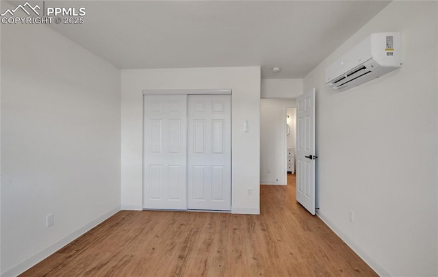 unfurnished bedroom with a wall mounted AC, light wood-style floors, baseboards, and a closet