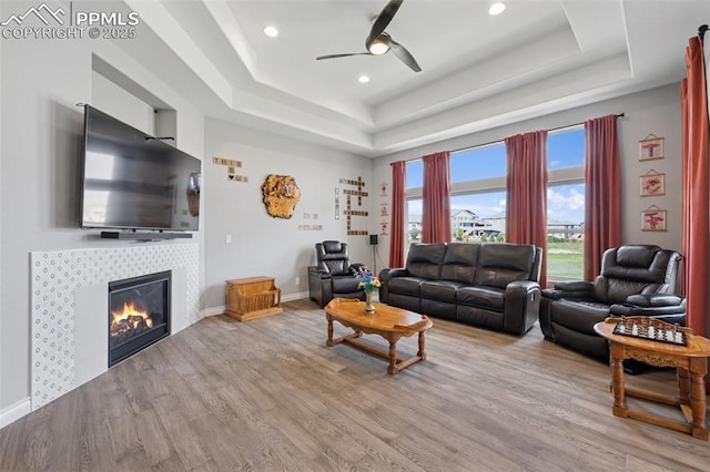 6949 Compass Bend Dr, Colorado Springs, CO 80927 - living room featuring a tray ceiling, light wood-style flooring, a ceiling fan, a tiled fireplace, and recessed lighting