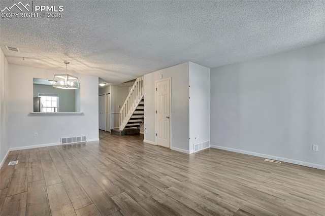 514 Shady Crest Cir, Colorado Springs, CO 80916 - unfurnished living room featuring a textured ceiling, wood finished floors, stairs, baseboards, and a chandelier