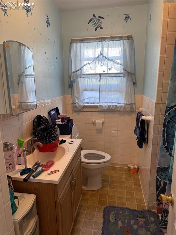 2531 Gunnison St, Colorado Springs, CO 80909 - bathroom featuring tile walls, toilet, vanity, wainscoting, and tile patterned floors