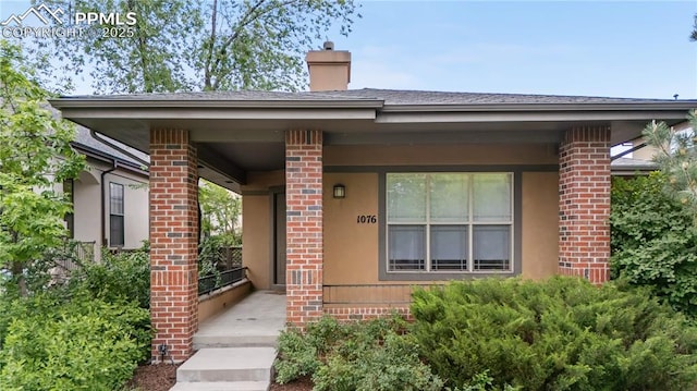 1076 Rosemary St, Denver, CO 80230 - entrance to property with a chimney, brick siding, covered porch, and a shingled roof
