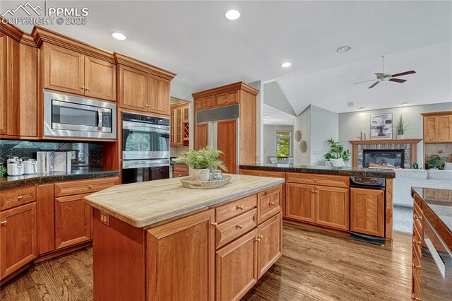 16150 Cliffrock Ct, Colorado Springs, CO 80921 - kitchen with built in appliances, a kitchen island, wood finished floors, a ceiling fan, and a glass covered fireplace