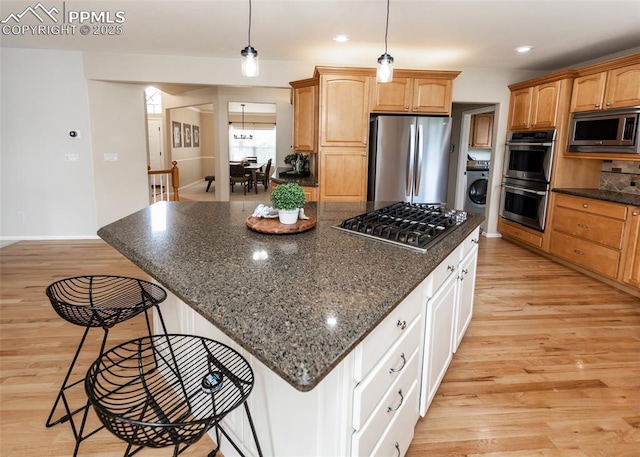 12515 Broad Oaks Dr, Colorado Springs, CO 80921 - kitchen featuring appliances with stainless steel finishes, washer / dryer, a breakfast bar, light wood finished floors, and a kitchen island