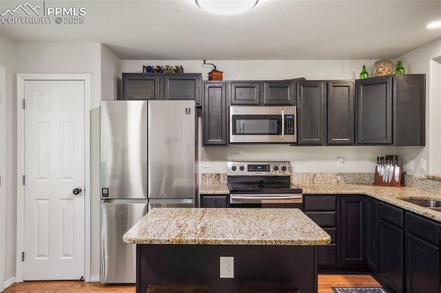 kitchen featuring stainless steel appliances, light stone counters, light wood-style flooring, and a center island