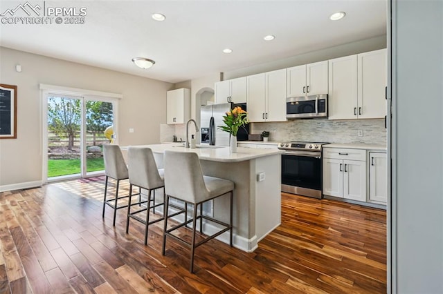 8445 Jacks Fork Dr, Colorado Springs, CO 80924 - kitchen with appliances with stainless steel finishes, dark wood finished floors, tasteful backsplash, a kitchen breakfast bar, and white cabinetry