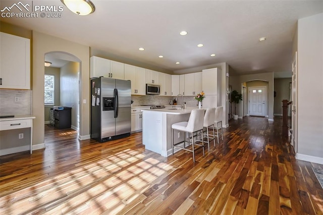 8445 Jacks Fork Dr, Colorado Springs, CO 80924 - kitchen featuring appliances with stainless steel finishes, arched walkways, decorative backsplash, wood finished floors, and recessed lighting