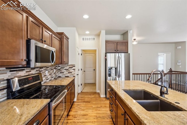 7663 Double Barrel Hts, Colorado Springs, CO 80923 - kitchen featuring stainless steel appliances, a sink, light wood-style floors, backsplash, and light stone counters