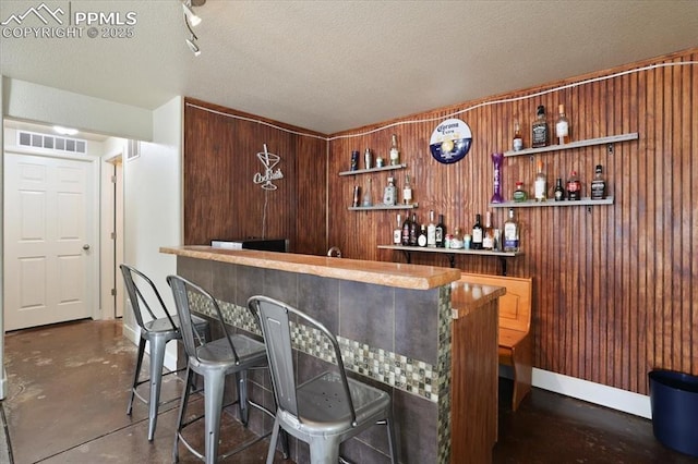 7719 Paca Pl, Fountain, CO 80817 - indoor wet bar featuring concrete flooring, baseboards, wood walls, and a textured ceiling
