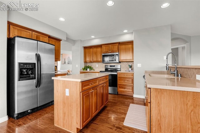 9883 Red Sage Dr, Colorado Springs, CO 80920 - kitchen featuring appliances with stainless steel finishes, a sink, a center island, arched walkways, and decorative backsplash