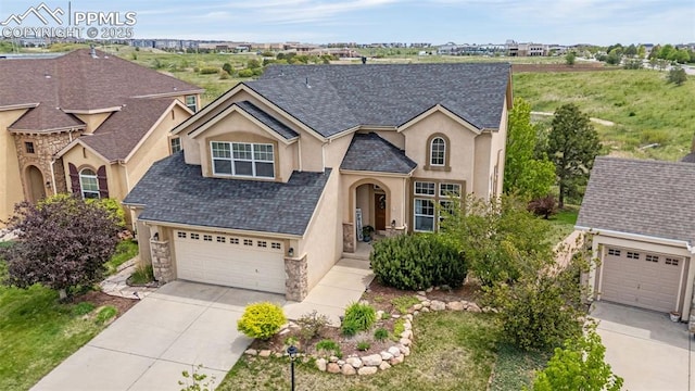 9883 Red Sage Dr, Colorado Springs, CO 80920 - view of front facade featuring stucco siding, stone siding, driveway, an attached garage, and roof with shingles