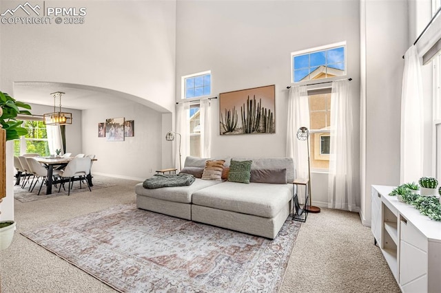 9883 Red Sage Dr, Colorado Springs, CO 80920 - carpeted living room with a high ceiling, arched walkways, baseboards, and a chandelier