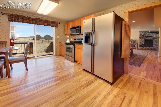 65 Sunshine Loop, Fairplay, CO 80440 - kitchen with stainless steel appliances, wallpapered walls, light wood-style flooring, dark countertops, and a fireplace