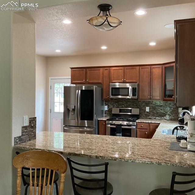 71 Mt Elbert Dr, Florissant, CO 80816 - kitchen with stainless steel appliances, light stone counters, a peninsula, backsplash, and recessed lighting
