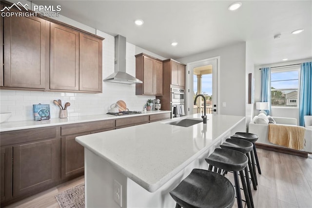 3071 Curly Grv, Colorado Springs, CO 80922 - kitchen with wall chimney range hood, a sink, stainless steel appliances, a kitchen bar, and decorative backsplash