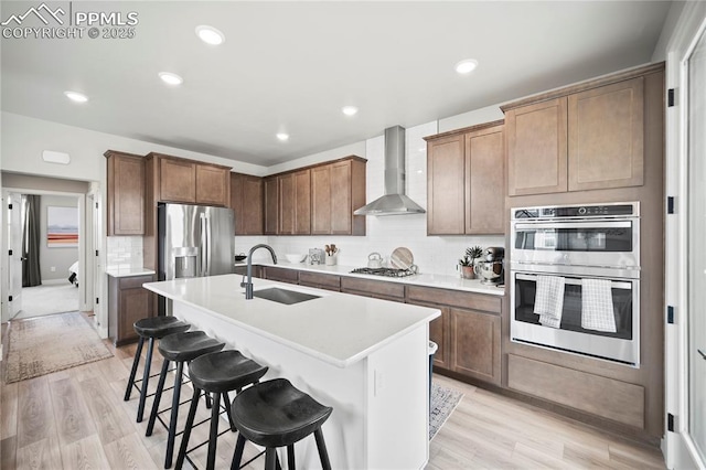 3071 Curly Grv, Colorado Springs, CO 80922 - kitchen featuring wall chimney range hood, a sink, stainless steel appliances, a breakfast bar, and light wood-type flooring