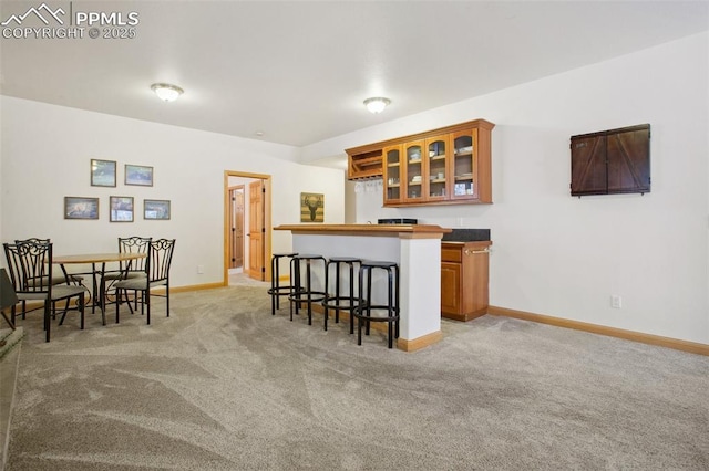 20190 Deer Shadow Way, Monument, CO 80132 - kitchen featuring a breakfast bar, light carpet, glass insert cabinets, brown cabinets, and baseboards
