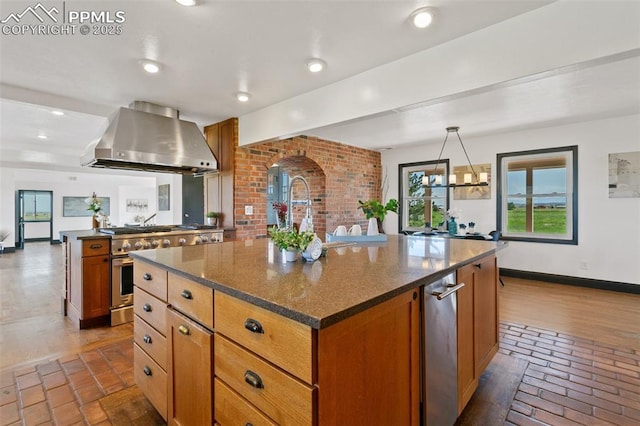 16030 Alta Plaza Cir, Peyton, CO 80831 - kitchen featuring wall chimney exhaust hood, stainless steel stove, brick flooring, brown cabinets, and a center island with sink