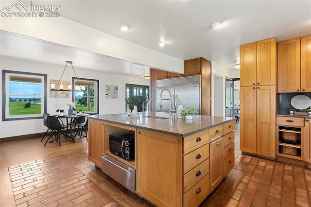 16030 Alta Plaza Cir, Peyton, CO 80831 - kitchen featuring stainless steel built in refrigerator, a warming drawer, black microwave, brick floors, and a center island with sink