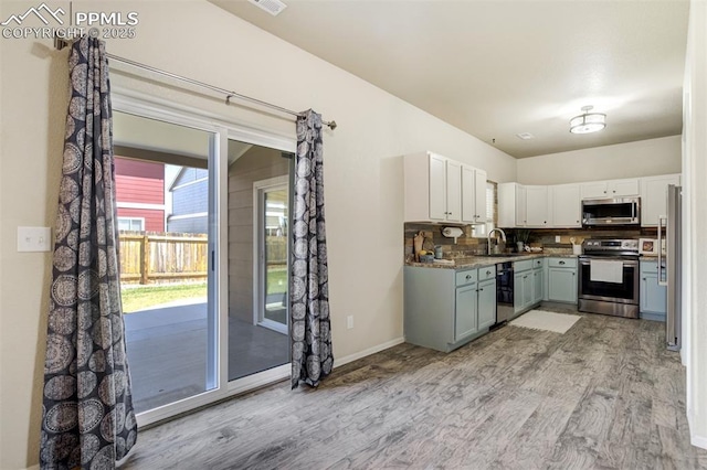 7923 Wagonwood Pl, Colorado Springs, CO 80908 - kitchen featuring appliances with stainless steel finishes, light wood-style floors, tasteful backsplash, a sink, and white cabinetry
