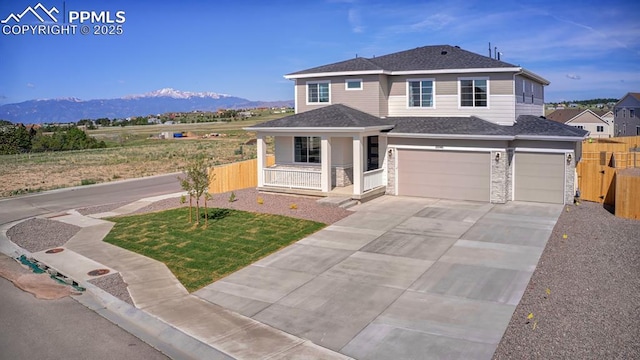10046 Keating Dr, Peyton, CO 80831 - view of front facade featuring covered porch, a mountain view, an attached garage, concrete driveway, and stone siding