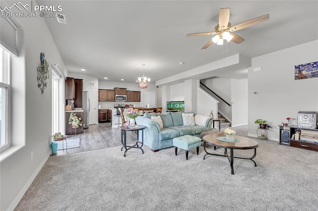 living room with light carpet, stairway, baseboards, a ceiling fan, and a chandelier