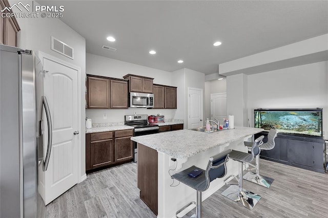 kitchen featuring stainless steel appliances, light wood-type flooring, light countertops, a kitchen bar, and dark brown cabinets