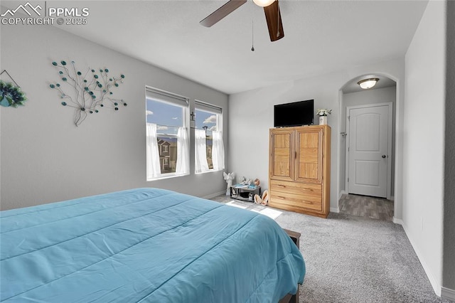 bedroom featuring light carpet, baseboards, arched walkways, and a ceiling fan