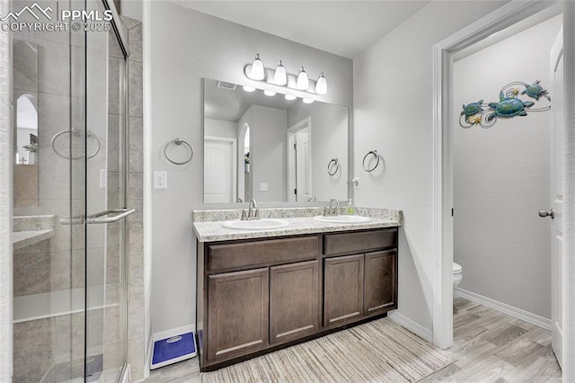 full bathroom featuring a shower stall, toilet, double vanity, baseboards, and wood finished floors