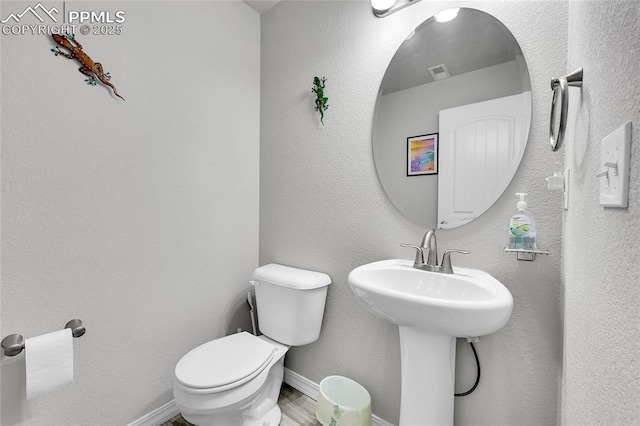 half bath featuring toilet, baseboards, a sink, and wood finished floors