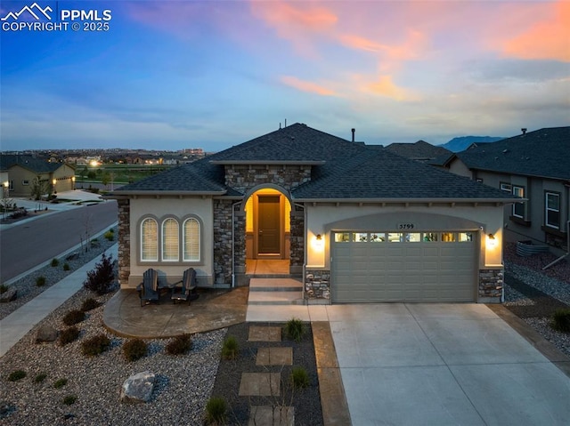 5799 Adkisson Pl, Colorado Springs, CO 80924 - french country style house with stone siding, an attached garage, driveway, stucco siding, and a shingled roof