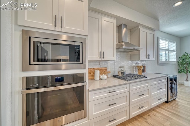 9473 Bugaboo Dr, Colorado Springs, CO 80924 - kitchen with stainless steel appliances, wall chimney exhaust hood, white cabinetry, light countertops, and a textured ceiling