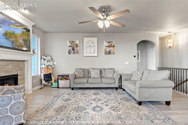 12879 Morning Creek Ln, Peyton, CO 80831 - living area with light wood-type flooring, a ceiling fan, arched walkways, a stone fireplace, and baseboards