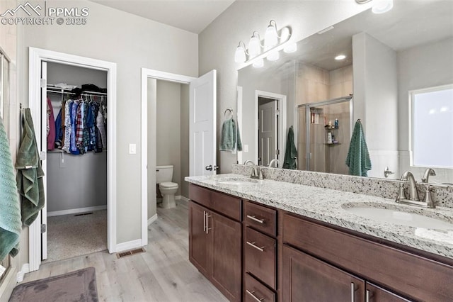 12879 Morning Creek Ln, Peyton, CO 80831 - bathroom featuring a shower stall, a walk in closet, wood finished floors, double vanity, and toilet