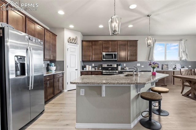 12879 Morning Creek Ln, Peyton, CO 80831 - kitchen featuring appliances with stainless steel finishes, a sink, light wood-type flooring, light stone countertops, and decorative backsplash