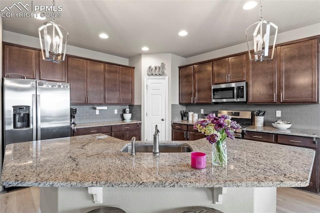 12879 Morning Creek Ln, Peyton, CO 80831 - kitchen with appliances with stainless steel finishes, a sink, dark brown cabinets, light stone counters, and a kitchen bar