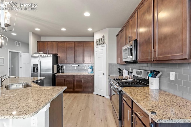 12879 Morning Creek Ln, Peyton, CO 80831 - kitchen featuring appliances with stainless steel finishes, a sink, decorative backsplash, light wood-style floors, and light stone counters