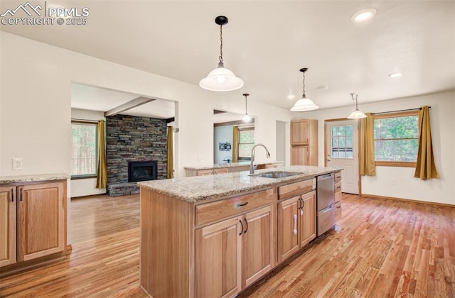 17990 Canterbury Dr, Monument, CO 80132 - kitchen with light wood-style floors, dishwasher, a kitchen island with sink, light stone counters, and a stone fireplace