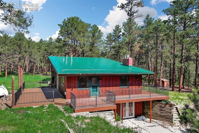17990 Canterbury Dr, Monument, CO 80132 - view of front facade with french doors, a chimney, a deck, board and batten siding, and a metal roof