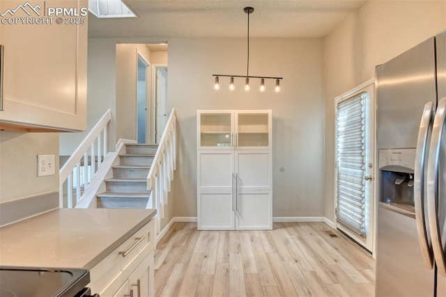 4472 Eastcrest Cir, Colorado Springs, CO 80916 - kitchen with stainless steel fridge with ice dispenser, light wood-style flooring, decorative light fixtures, white cabinets, and baseboards