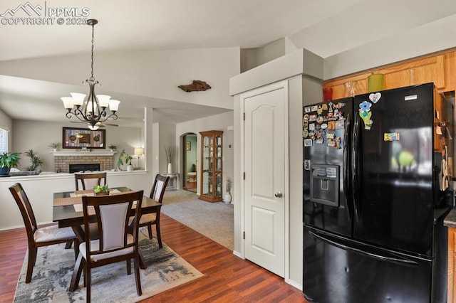 6557 Many Moon Dr, Colorado Springs, CO 80923 - dining room with a chandelier, a brick fireplace, dark wood-style floors, arched walkways, and high vaulted ceiling
