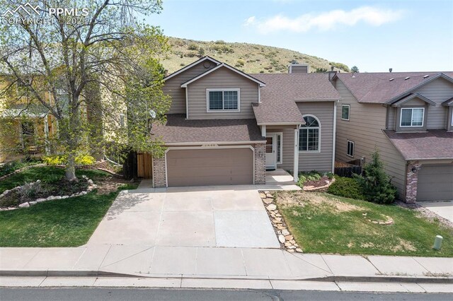 7435 Julynn Rd, Colorado Springs, CO 80919 - view of front of house with a garage, concrete driveway, roof with shingles, a front lawn, and brick siding