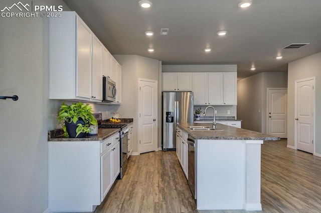 10144 Bluffstone Ct, Peyton, CO 80831 - kitchen with appliances with stainless steel finishes, a sink, wood finished floors, an island with sink, and white cabinetry