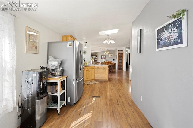 9180 S Rush Rd, Rush, CO 80833 - kitchen featuring light brown cabinets, freestanding refrigerator, a peninsula, light wood-type flooring, and a chandelier