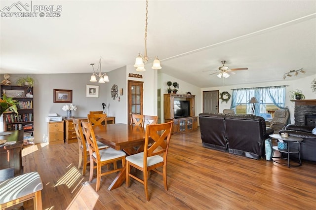 9180 S Rush Rd, Rush, CO 80833 - dining room with wood finished floors, a ceiling fan, a chandelier, vaulted ceiling, and a stone fireplace